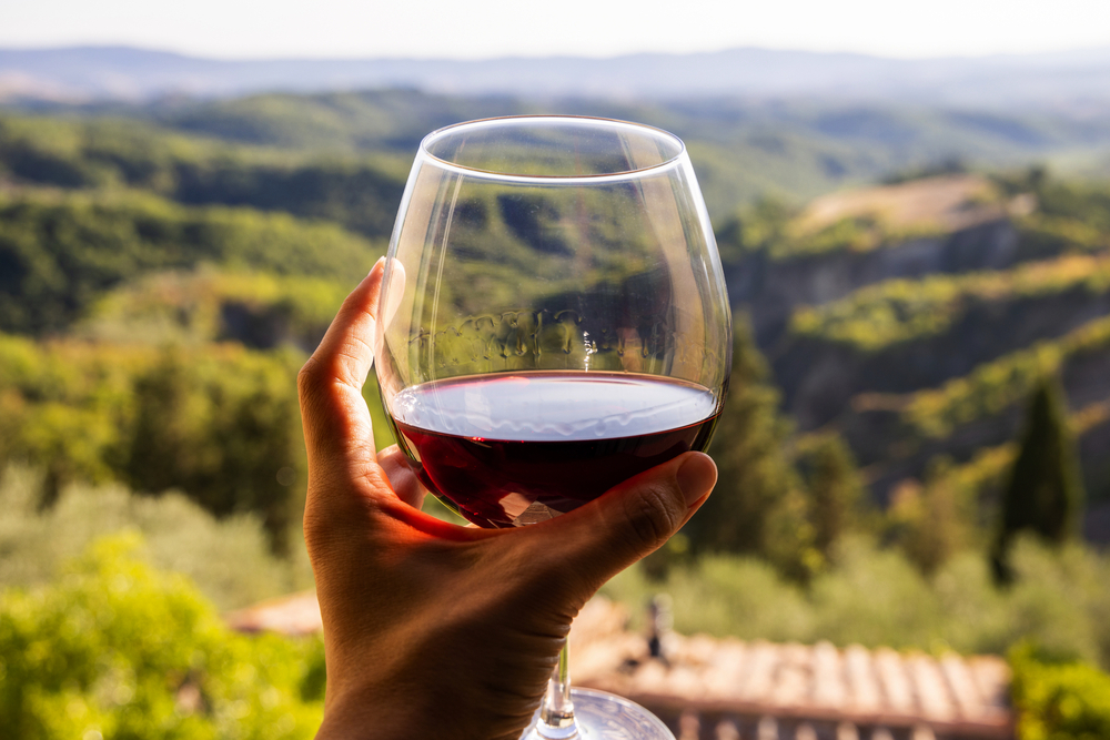 Frau hält ein Glas Rotwein in der Hand, im Hintergrund die Landschaft Italiens